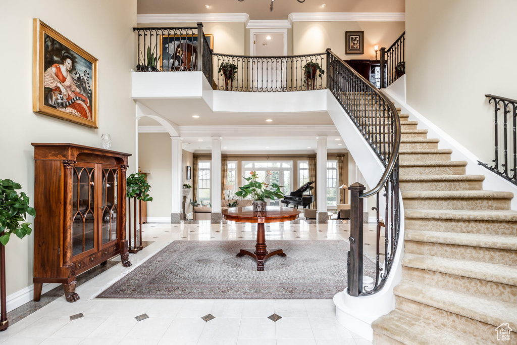 Foyer entrance featuring light tile flooring, decorative columns, crown molding, and a towering ceiling