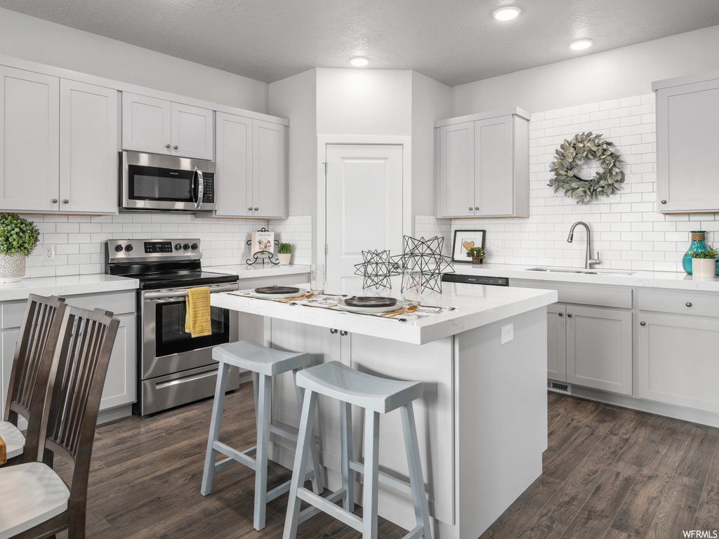 kitchen with a center island, a kitchen breakfast bar, microwave, electric range oven, light countertops, dark parquet floors, and white cabinets