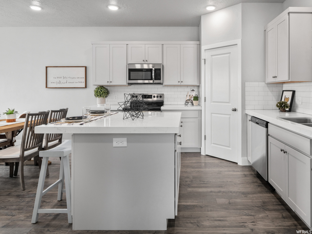 kitchen featuring a kitchen bar, range oven, stainless steel microwave, dishwasher, light countertops, white cabinetry, and dark hardwood flooring