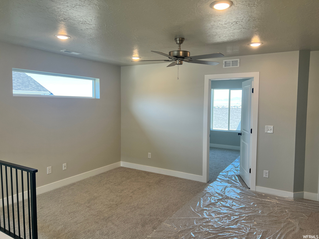 Spare room with ceiling fan, light carpet, and a textured ceiling