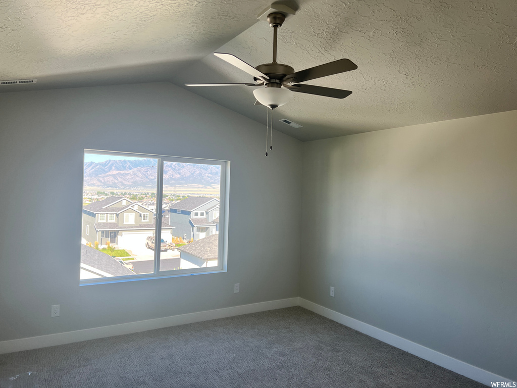 Empty room featuring a textured ceiling, light carpet, plenty of natural light, ceiling fan, and lofted ceiling
