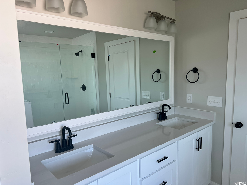 Bathroom featuring a shower with door, double sink vanity, and mirror