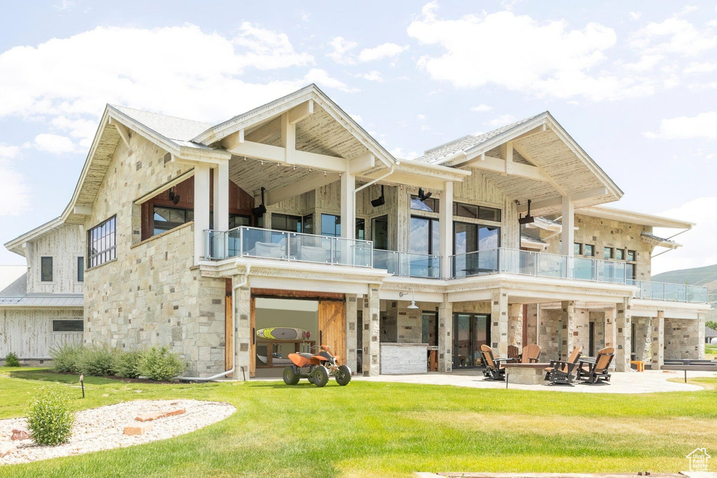 Back of house featuring a balcony, an outdoor fire pit, a patio, a yard, and stone siding