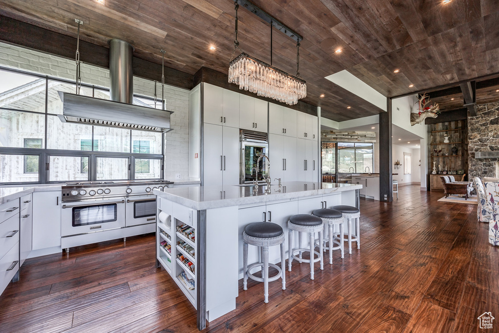 Kitchen with range with two ovens, wooden ceiling, wall chimney exhaust hood, light countertops, and dark wood-style floors
