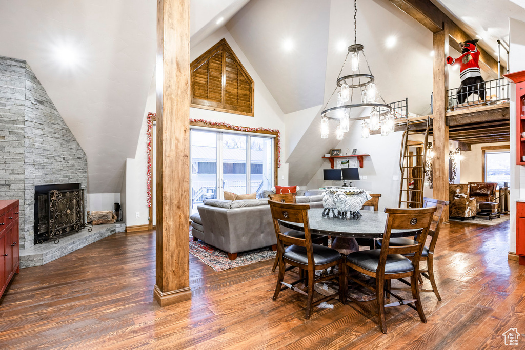 Dining area featuring a chandelier, high vaulted ceiling, wood finished floors, and a stone fireplace