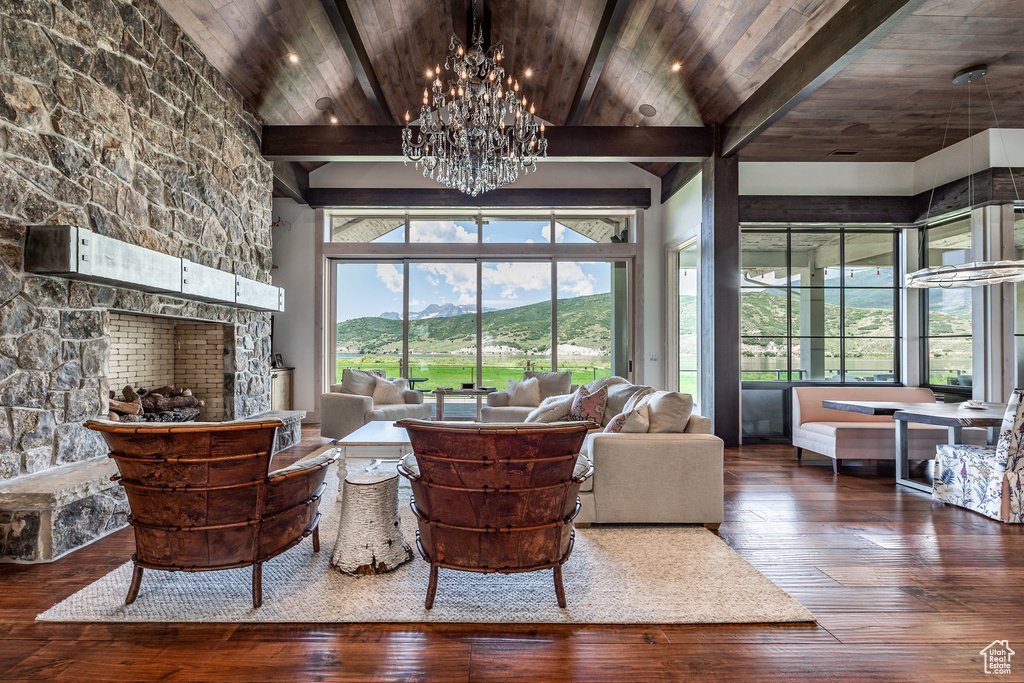 Living area featuring hardwood / wood-style flooring, a chandelier, beamed ceiling, wood ceiling, and a stone fireplace