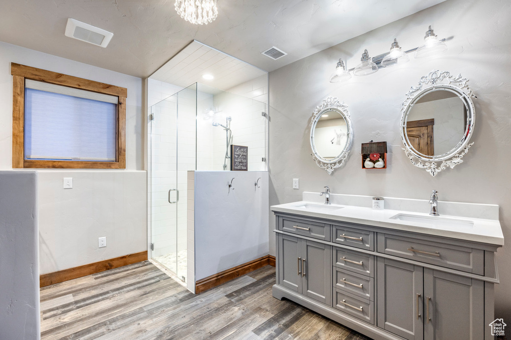 Bathroom with wood finished floors, baseboards, a shower stall, double vanity, and a chandelier