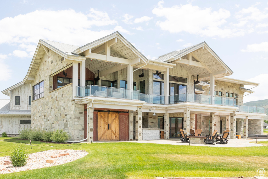 Rear view of property featuring a balcony, an outdoor fire pit, a patio area, a lawn, and stone siding