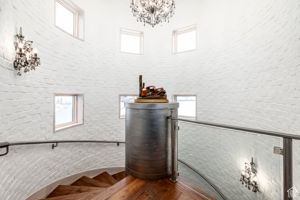 Stairway with a high ceiling, a chandelier, brick wall, healthy amount of natural light, and wood finished floors