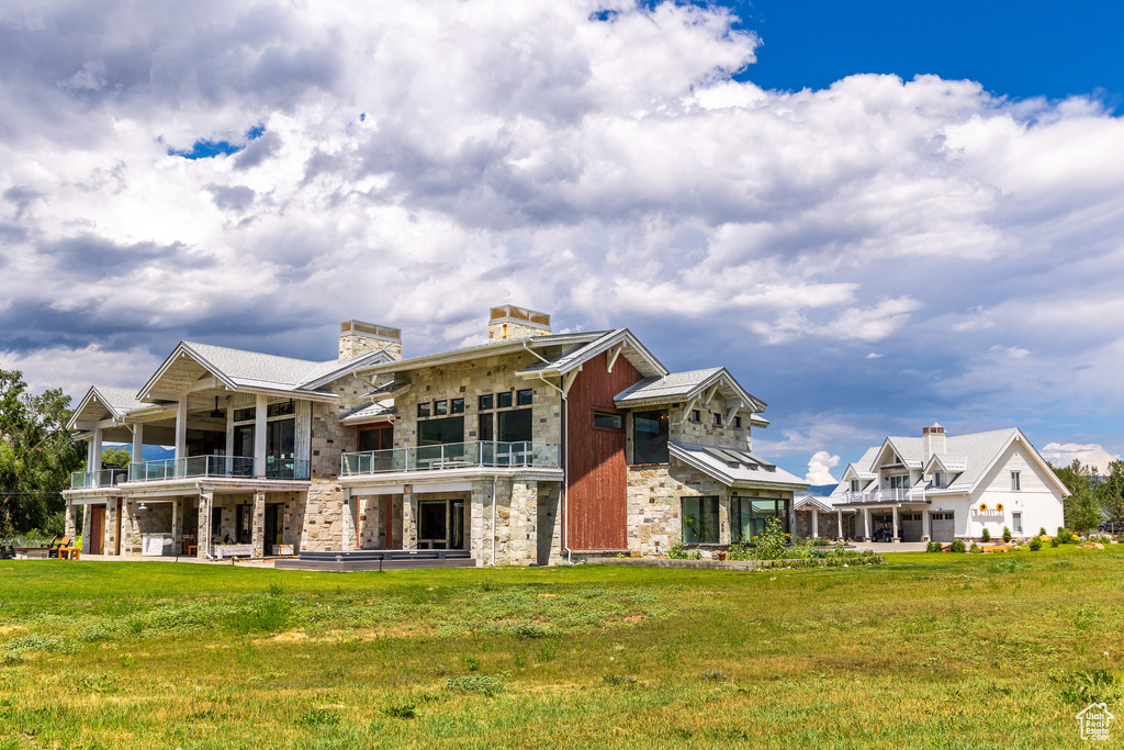 Rear view of property with a balcony, a lawn, stone siding, and a chimney