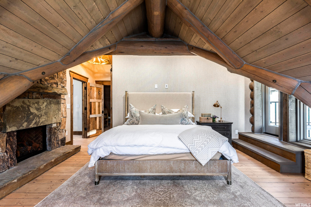 Bedroom with light hardwood / wood-style flooring, lofted ceiling with beams, and a stone fireplace