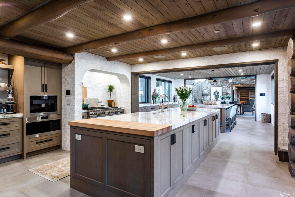 Kitchen with beamed ceiling, a kitchen island with sink, and double oven