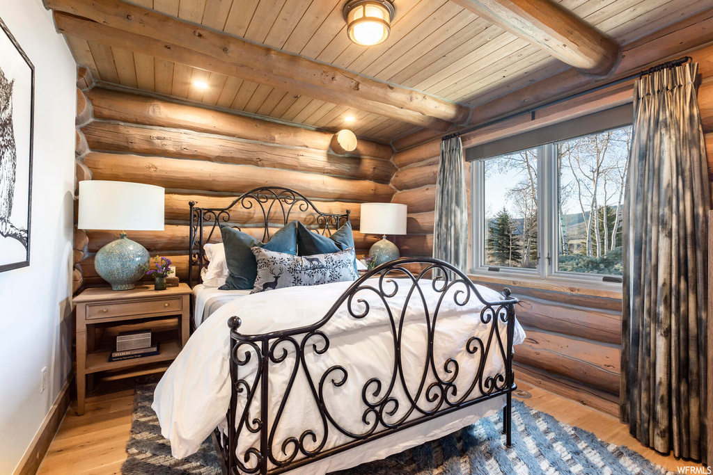 Bedroom with wooden ceiling, beam ceiling, rustic walls, and light hardwood / wood-style floors