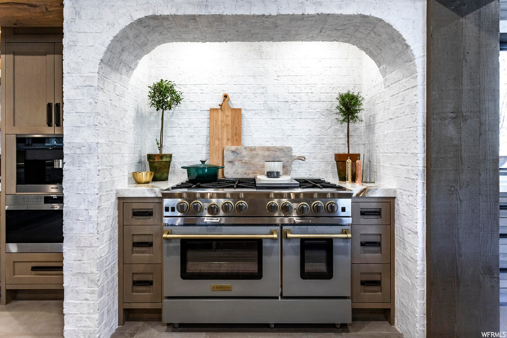 Kitchen with light tile flooring, range with two ovens, double wall oven, and brick wall