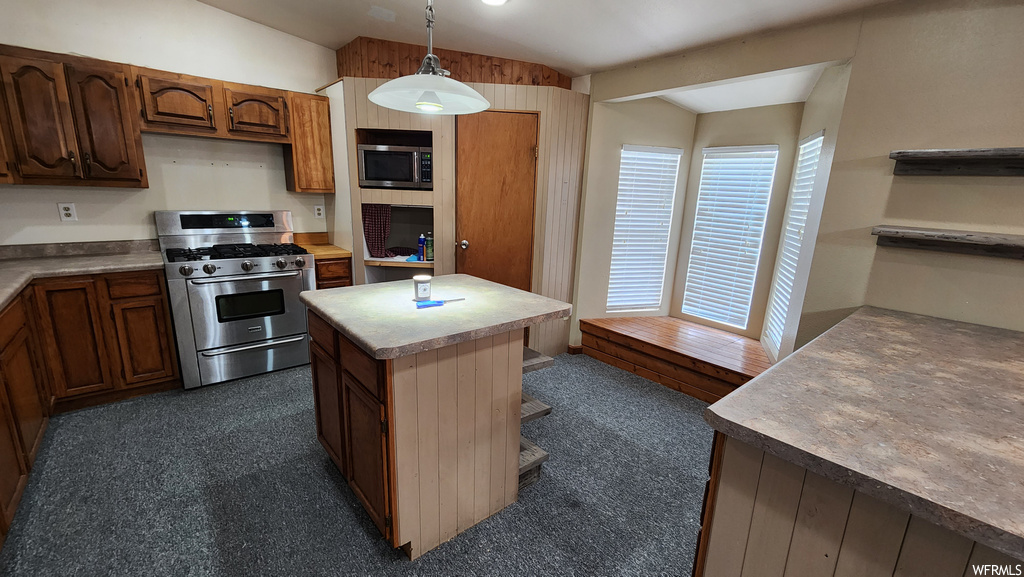 Kitchen with gas range oven, microwave, light countertops, dark flooring, and pendant lighting