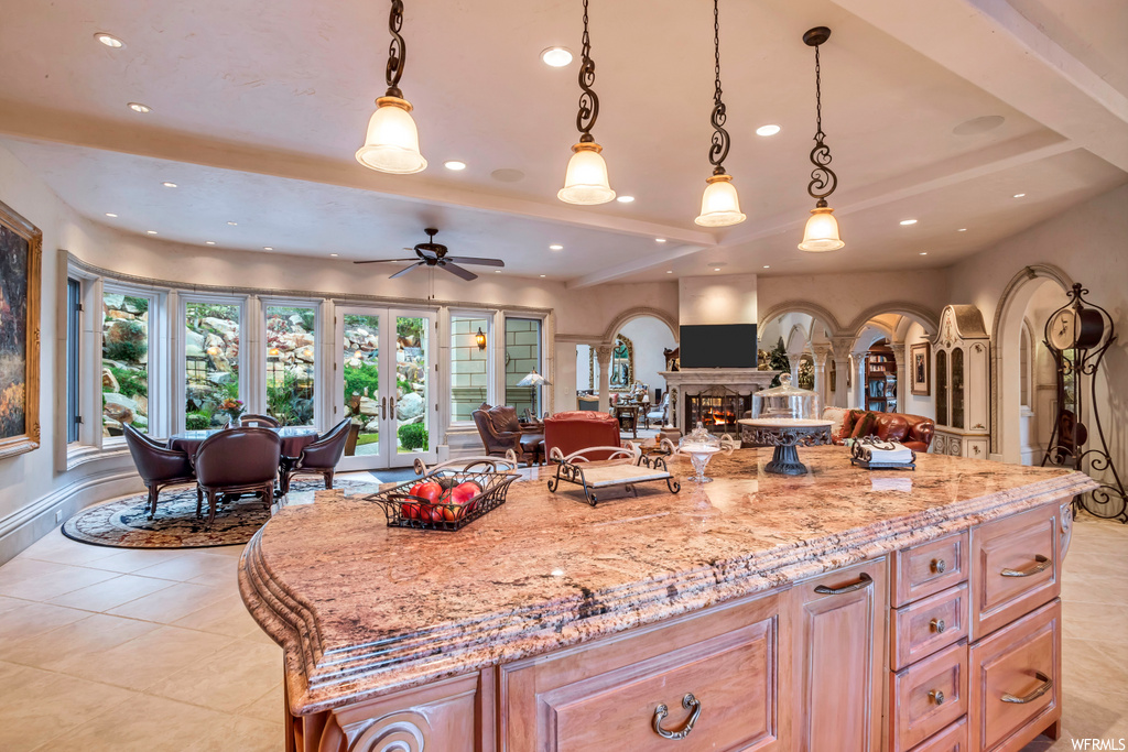 kitchen with a fireplace, a ceiling fan, TV, pendant lighting, light tile floors, and light stone countertops