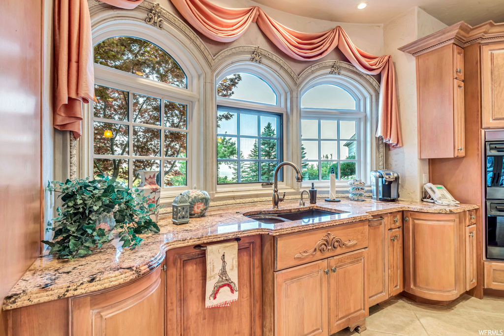 kitchen with a wealth of natural light, double oven, brown cabinetry, light tile flooring, and light stone countertops