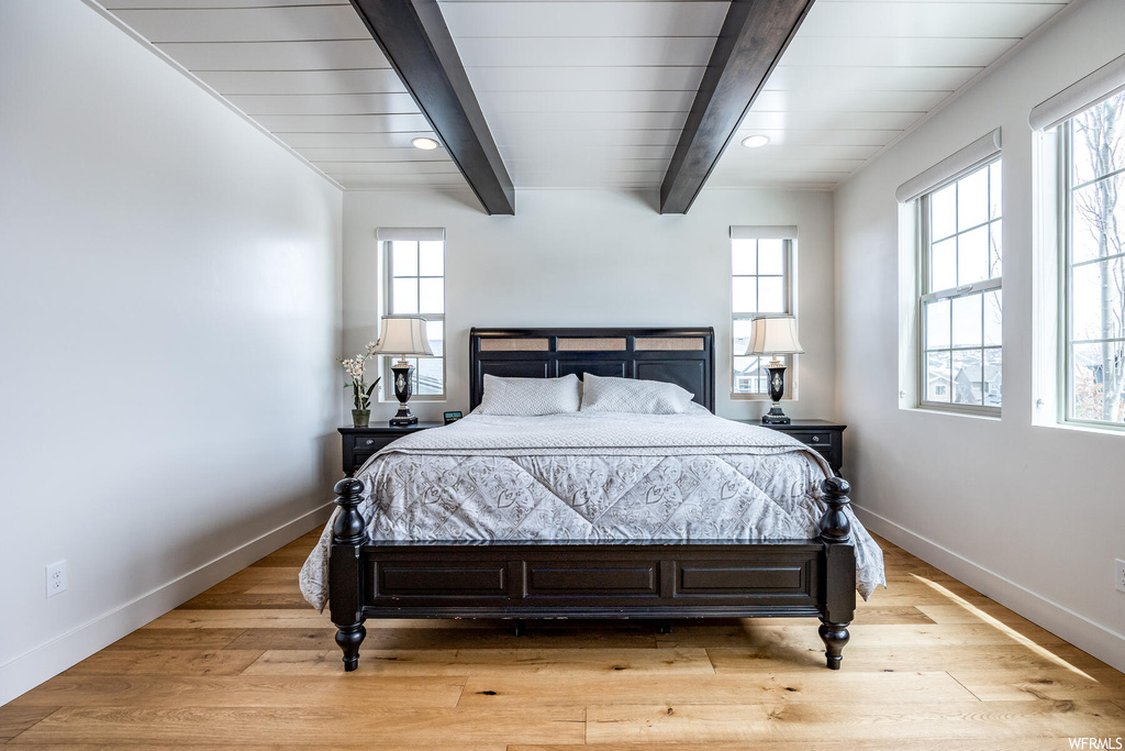 Hardwood floored bedroom featuring natural light and wood beam ceiling