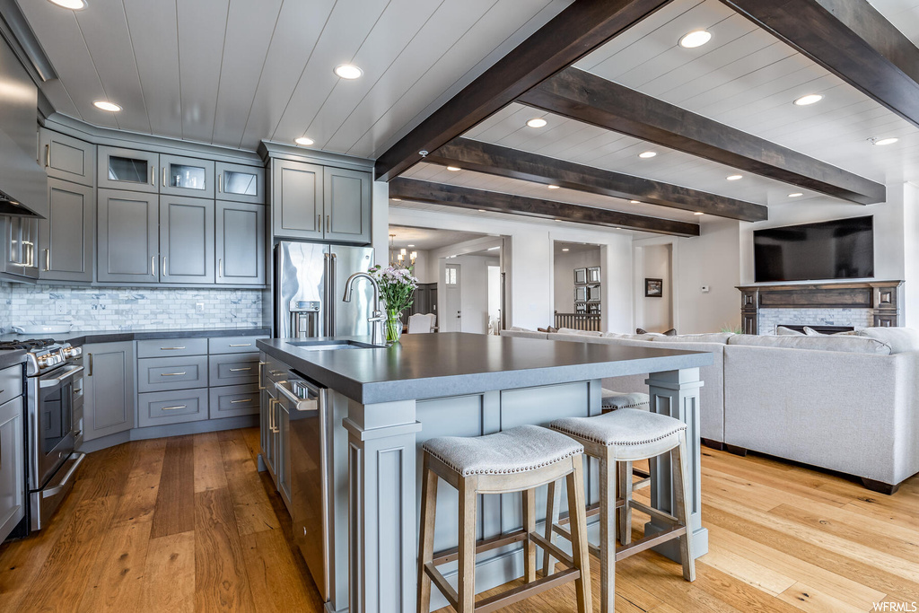 Kitchen featuring a breakfast bar area, wood beam ceiling, TV, fume extractor, refrigerator, range oven, light countertops, and light parquet floors