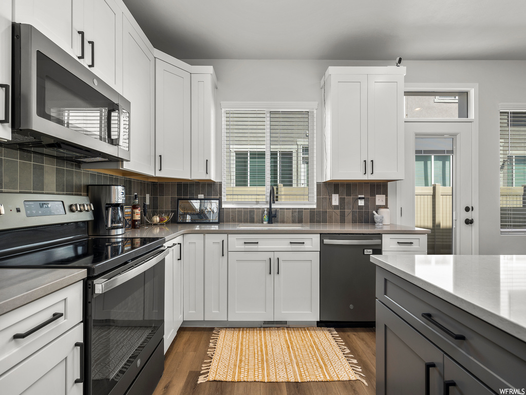kitchen featuring a wealth of natural light, electric range oven, dishwasher, microwave, light countertops, white cabinetry, and light hardwood floors