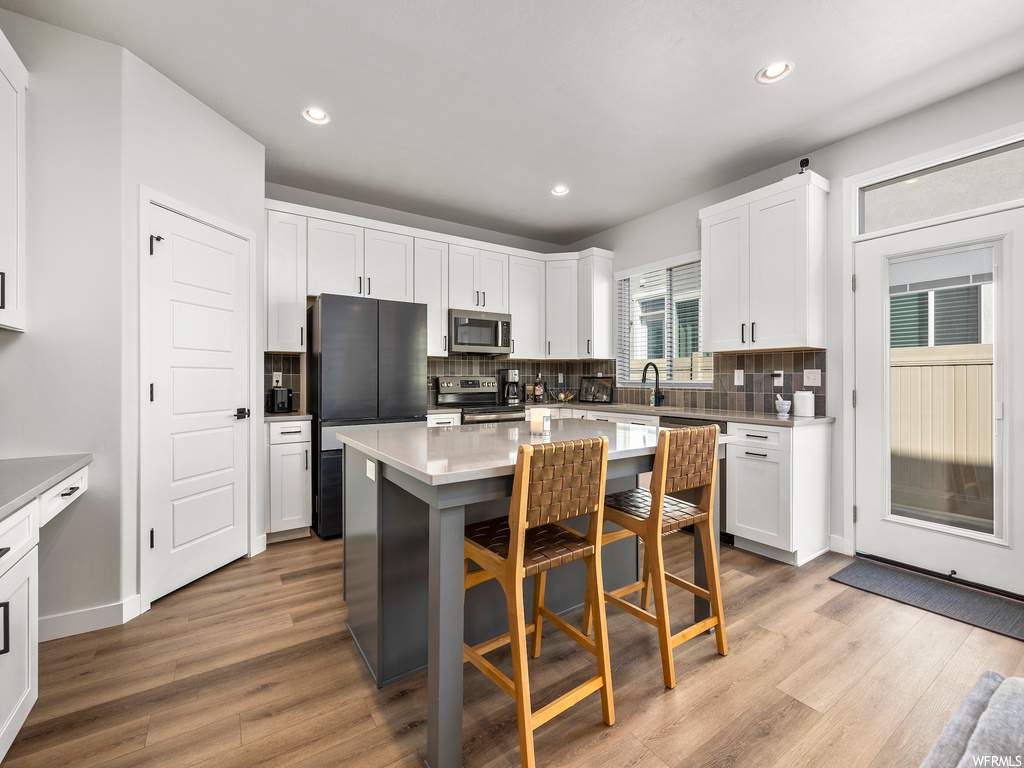 kitchen featuring natural light, hardwood flooring, refrigerator, microwave, range oven, white cabinetry, and light countertops