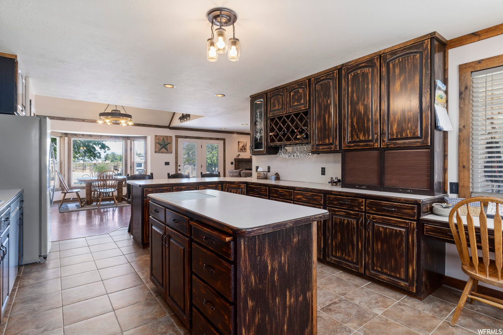 kitchen featuring a center island, natural light, refrigerator, light tile floors, and dark brown cabinetry