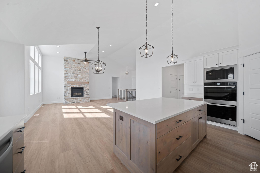 Kitchen featuring appliances with stainless steel finishes, a stone fireplace, a center island, light hardwood / wood-style floors, and white cabinets