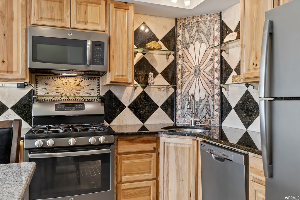Kitchen with stainless steel dishwasher, refrigerator, microwave, gas range oven, and dark stone countertops