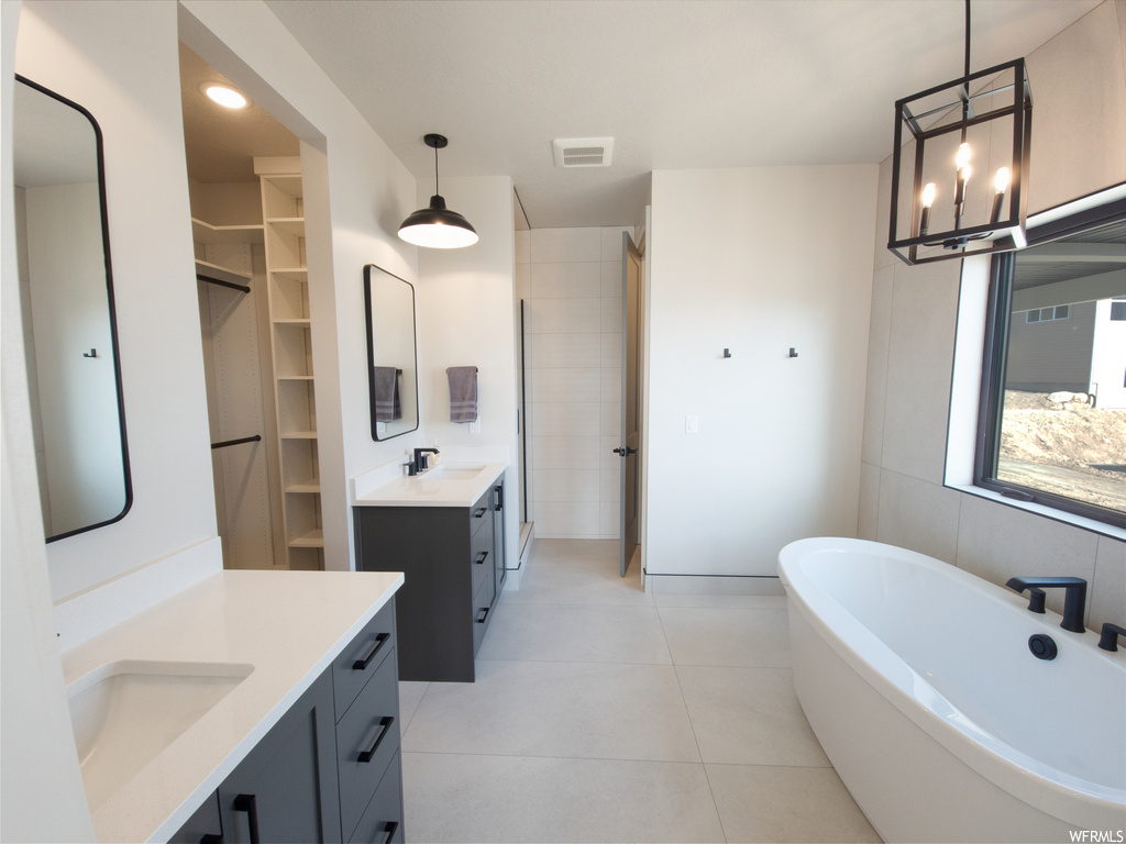 Bathroom with mirror, light tile floors, double large sink vanity, tile walls, and a bath to relax in