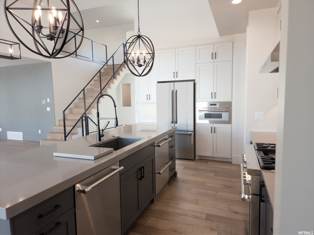 Kitchen featuring stainless steel appliances, white cabinets, wood-type flooring, light countertops, and premium range hood