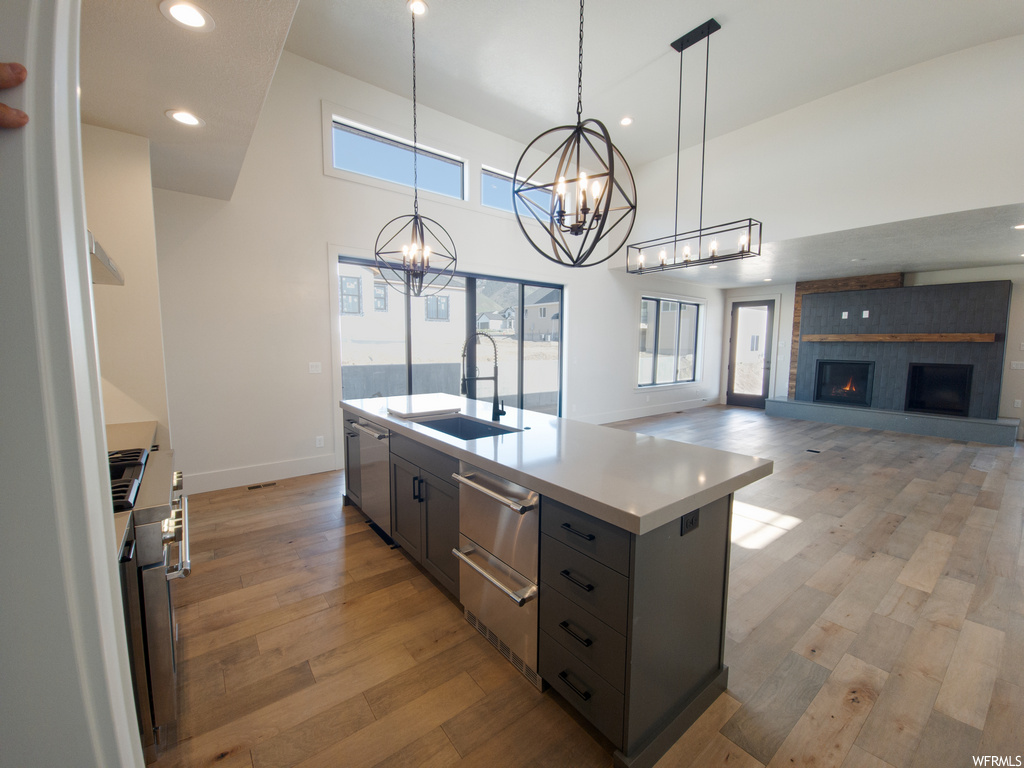 Kitchen with stainless steel dishwasher, decorative light fixtures, range, a fireplace, light countertops, light hardwood flooring, and a high ceiling