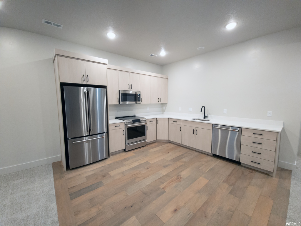 Kitchen with white cabinets, light countertops, light hardwood floors, and stainless steel appliances