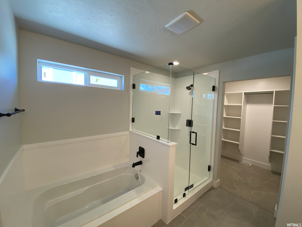 Bathroom with tile floors, shower with separate bathtub, and a textured ceiling