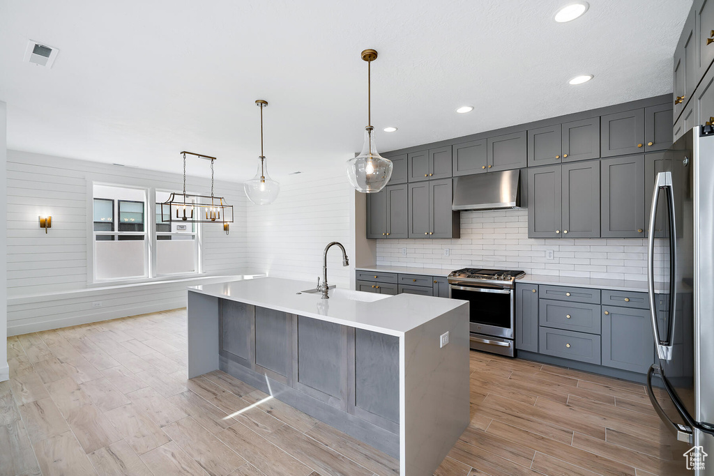 Kitchen featuring gray cabinetry, hanging light fixtures, appliances with stainless steel finishes, and a center island with sink