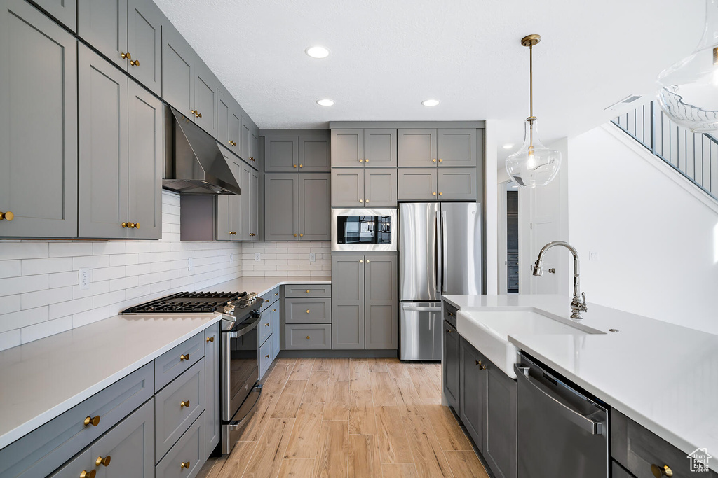 Kitchen with appliances with stainless steel finishes, gray cabinets, hanging light fixtures, and light wood-type flooring