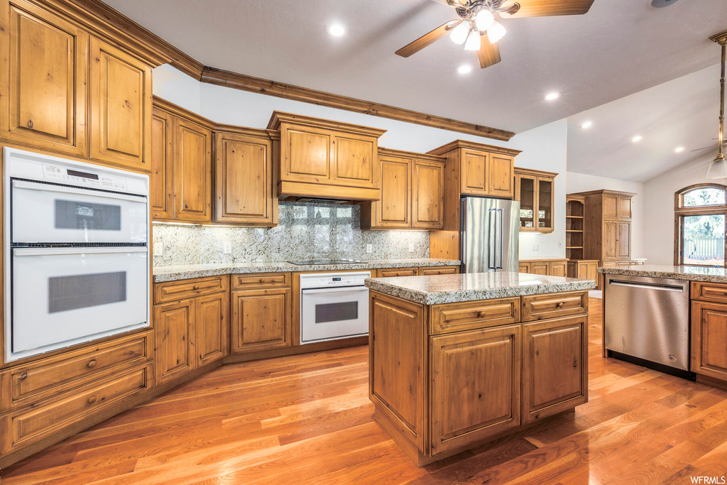 Kitchen with vaulted ceiling, light hardwood / wood-style floors, appliances with stainless steel finishes, a center island, and ceiling fan