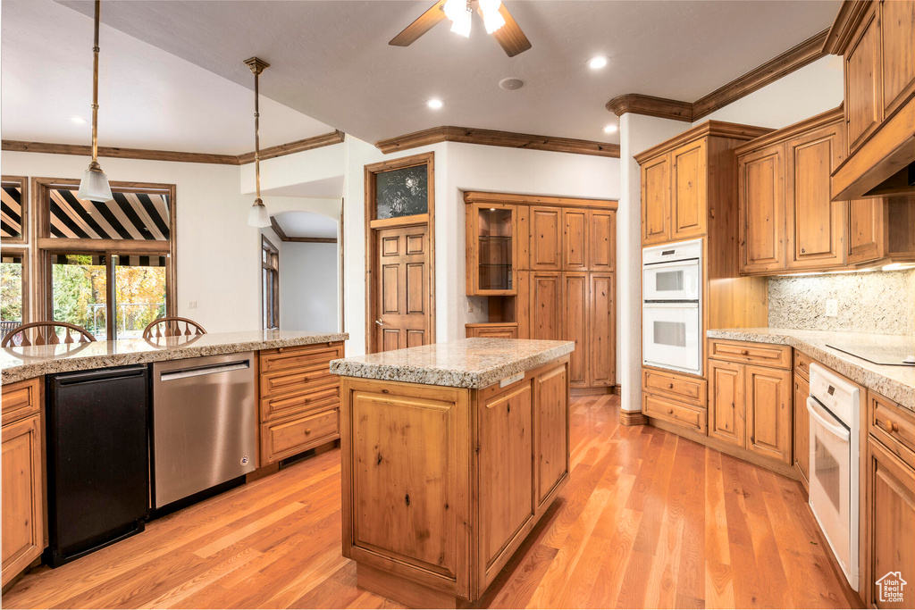 Kitchen featuring ceiling fan, light wood-type flooring, stainless steel dishwasher, decorative light fixtures, and a center island