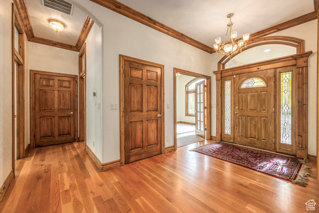 Foyer entrance featuring a chandelier, plenty of natural light, light wood-type flooring, and crown molding