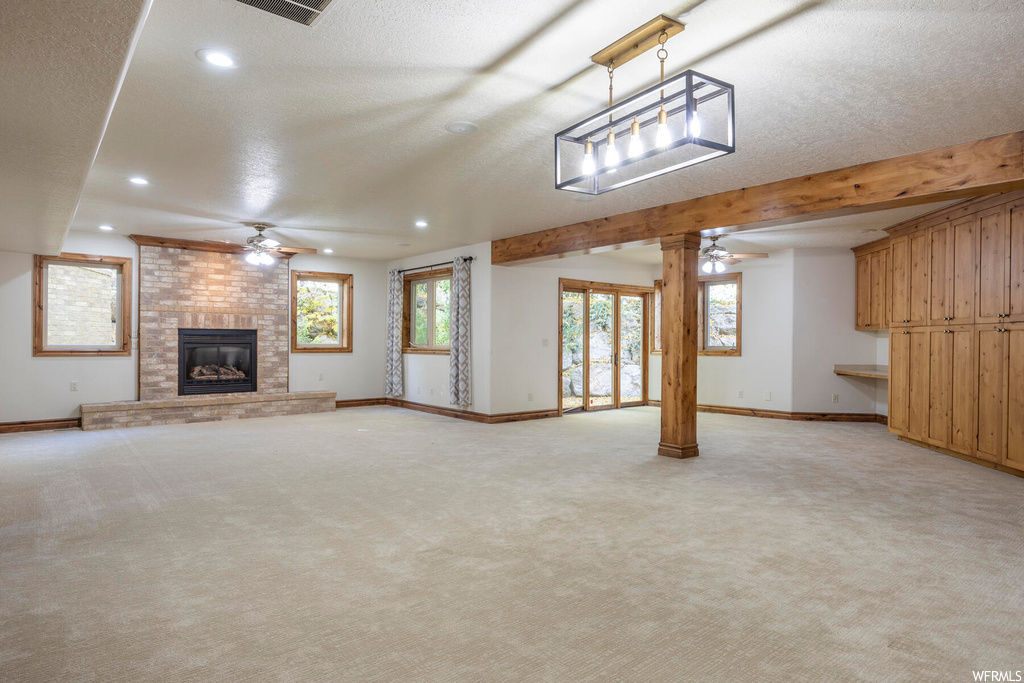 Unfurnished living room featuring light colored carpet, ceiling fan, a fireplace, and brick wall