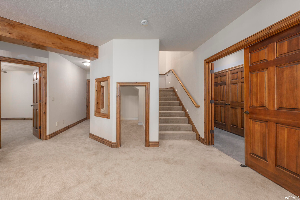 Foyer entrance featuring light carpet, beam ceiling, and a textured ceiling