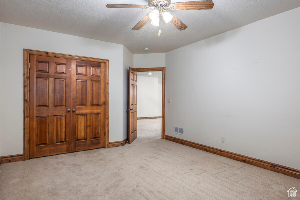 Unfurnished bedroom with light colored carpet, ceiling fan, and a textured ceiling