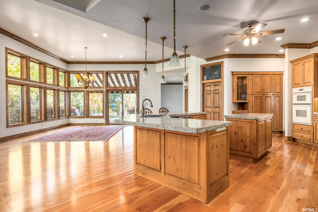 Kitchen featuring sink, ceiling fan with notable chandelier, hanging light fixtures, light hardwood / wood-style floors, and an island with sink