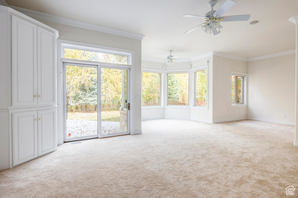 Empty room featuring a healthy amount of sunlight, light colored carpet, ceiling fan, and crown molding