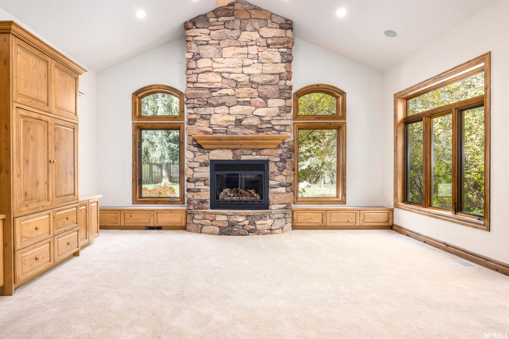 Unfurnished living room featuring high vaulted ceiling, a fireplace, and light carpet