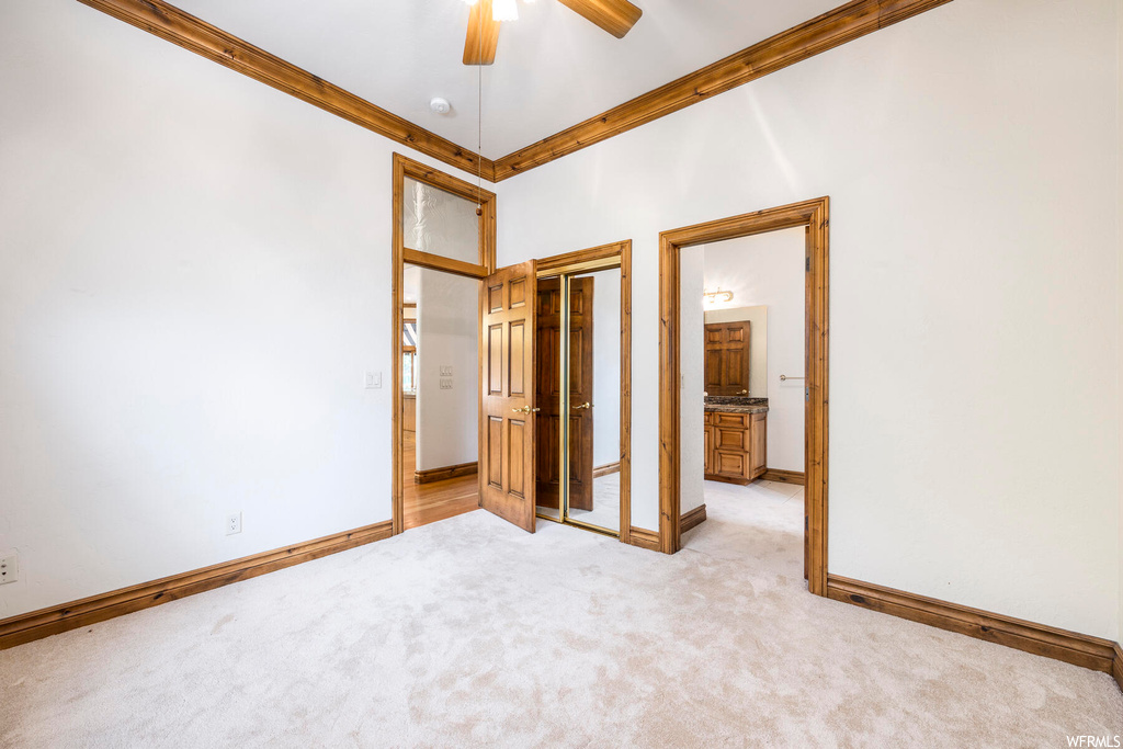 Unfurnished bedroom featuring crown molding, a towering ceiling, a closet, ceiling fan, and light colored carpet