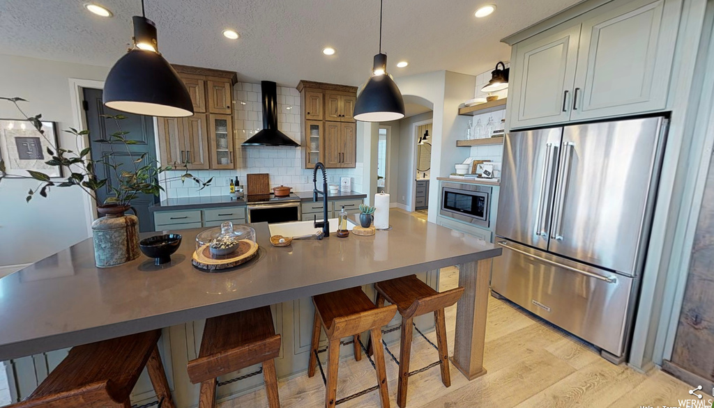 Kitchen featuring a kitchen breakfast bar, refrigerator, microwave, range hood, pendant lighting, brown cabinets, light floors, and dark countertops