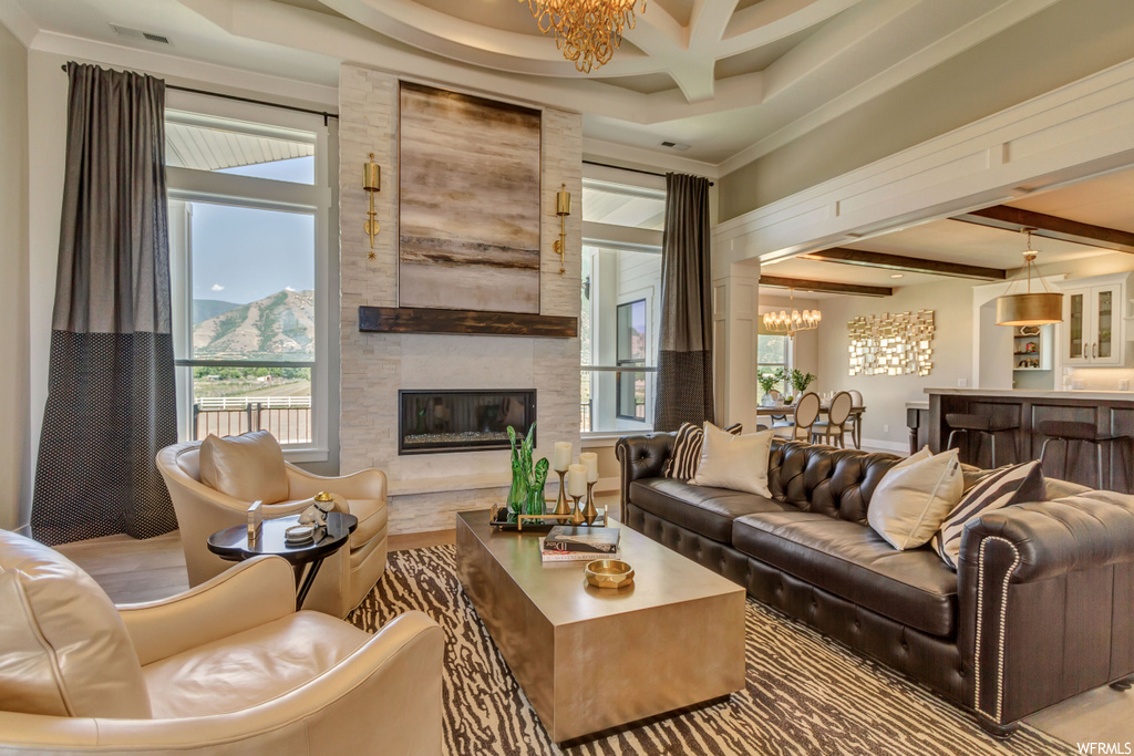 Living room with a kitchen bar, coffered ceiling, beamed ceiling, a notable chandelier, a fireplace, and natural light
