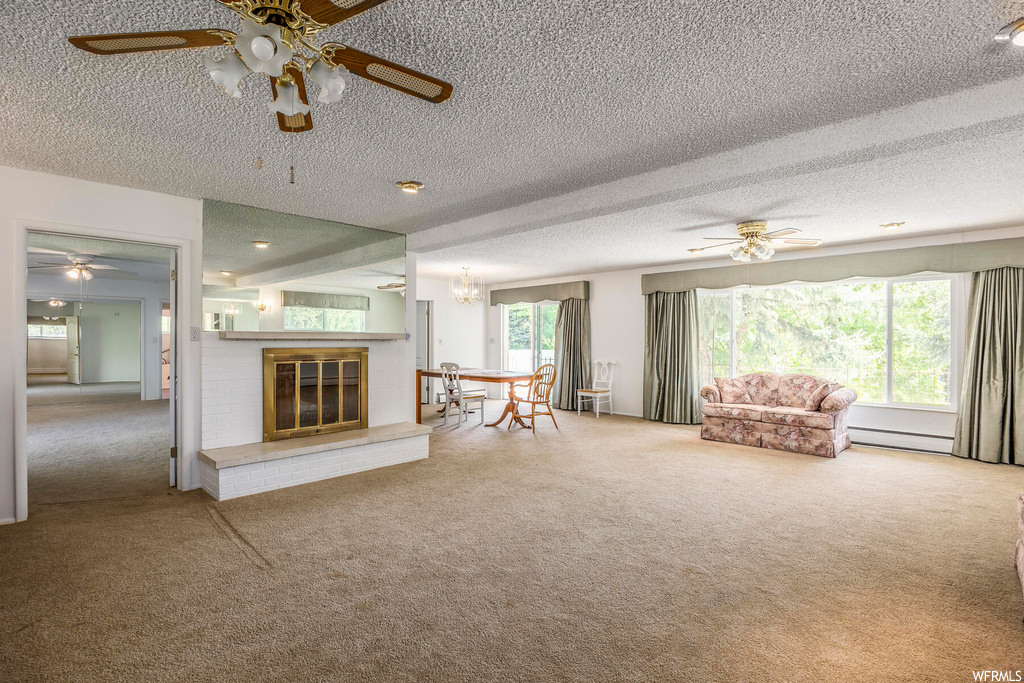 Carpeted living room featuring a textured ceiling, a fireplace, a wealth of natural light, baseboard heating, and ceiling fan