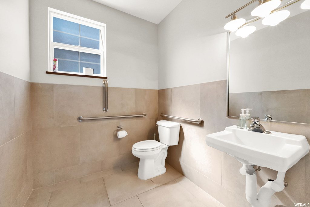 Bathroom featuring mirror, tile walls, sink, and light tile floors