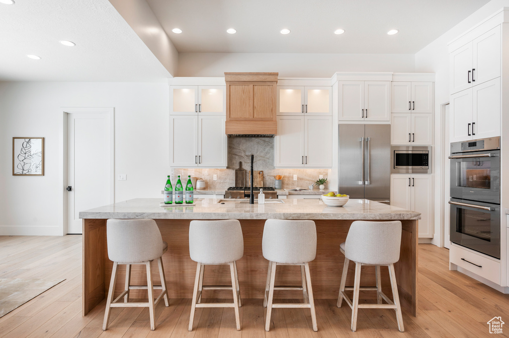 Kitchen featuring light hardwood / wood-style flooring, a center island with sink, white cabinets, and built in appliances
